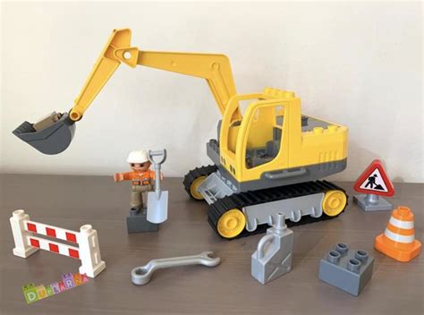 Ilustrace sady LEGO DUPLO Náklaďák a pásový bagr ukazující náklaďák, bagr, figurky dělníků a balvan.