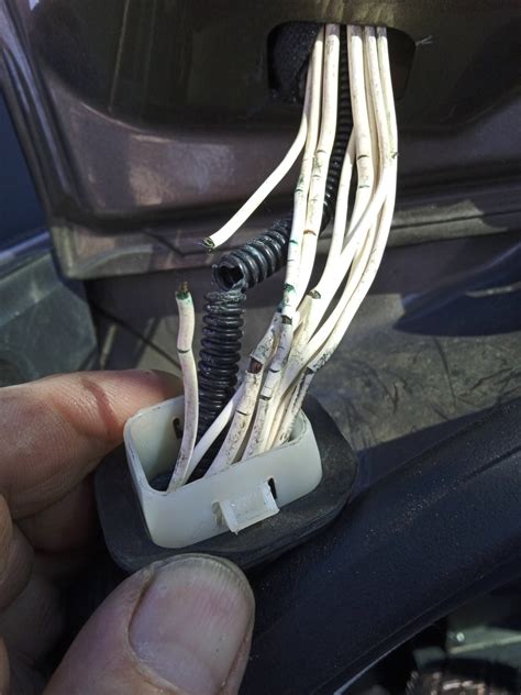 Detailní fotografie poškozeného kabelového svazku ve dveřích s viditelnými přerušenými vodiči