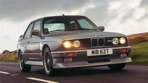 Obrázek BMW E30 M3 s detailním pohledem na přední část, kde jsou vidět blatníky a nárazník.