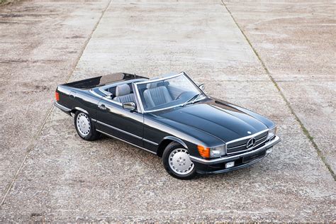 Stylizovaný snímek vozu Mercedes-Benz R107 s otevřenou střechou na pozadí luxusního prostředí